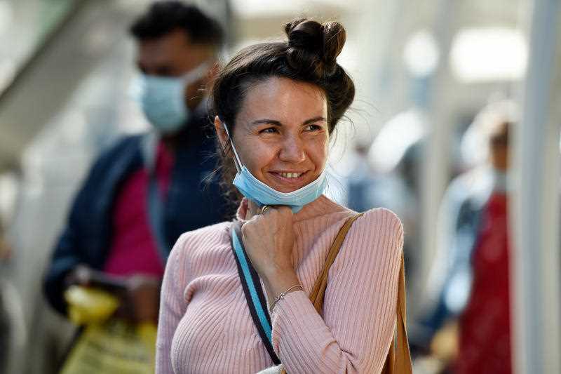 An Australian resident returning from India smiles at media as she is ushered towards waiting busses for the beginning of her 14-day imposed quarantine, after arriving at Sydney International Airport in Sydney.