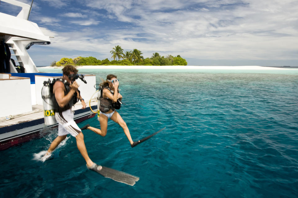 Two people jumping into the water from a boat to go snorkeling