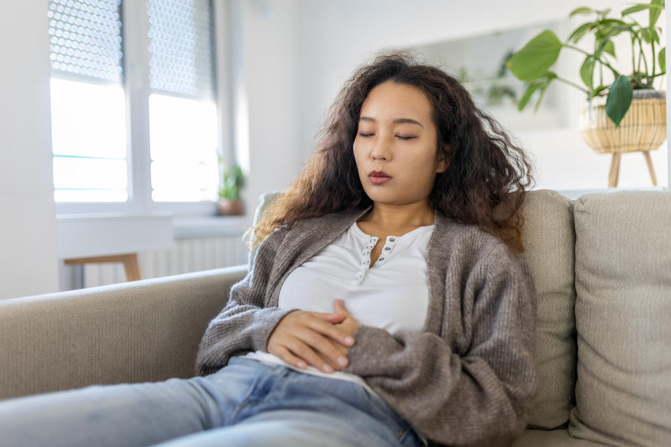 A woman sitting on the couch with her eyes closed and her arms resting on her abdomen