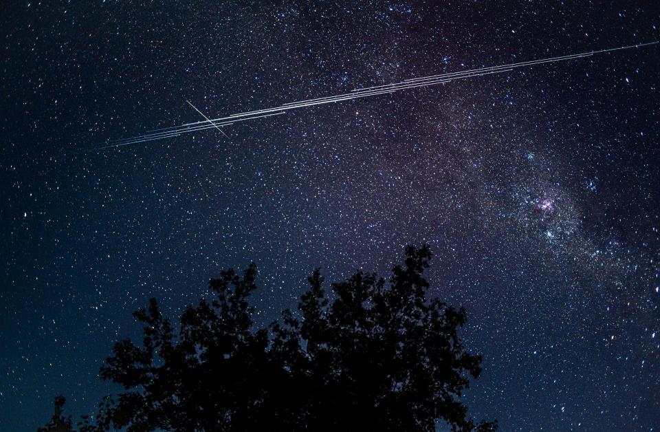 Photo of the night sky with Starlink satellites making a white streak across the sky as they orbit Earth.