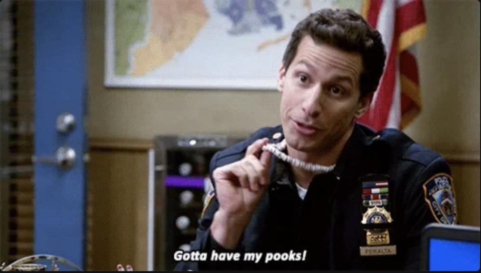 Andy Samberg, dressed as a police officer, holds a necklace, mouthing 