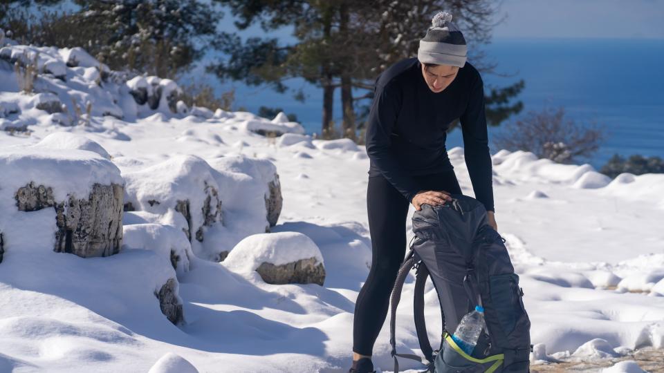 A hiker in thermal underwear rummages through his backpack in the snow