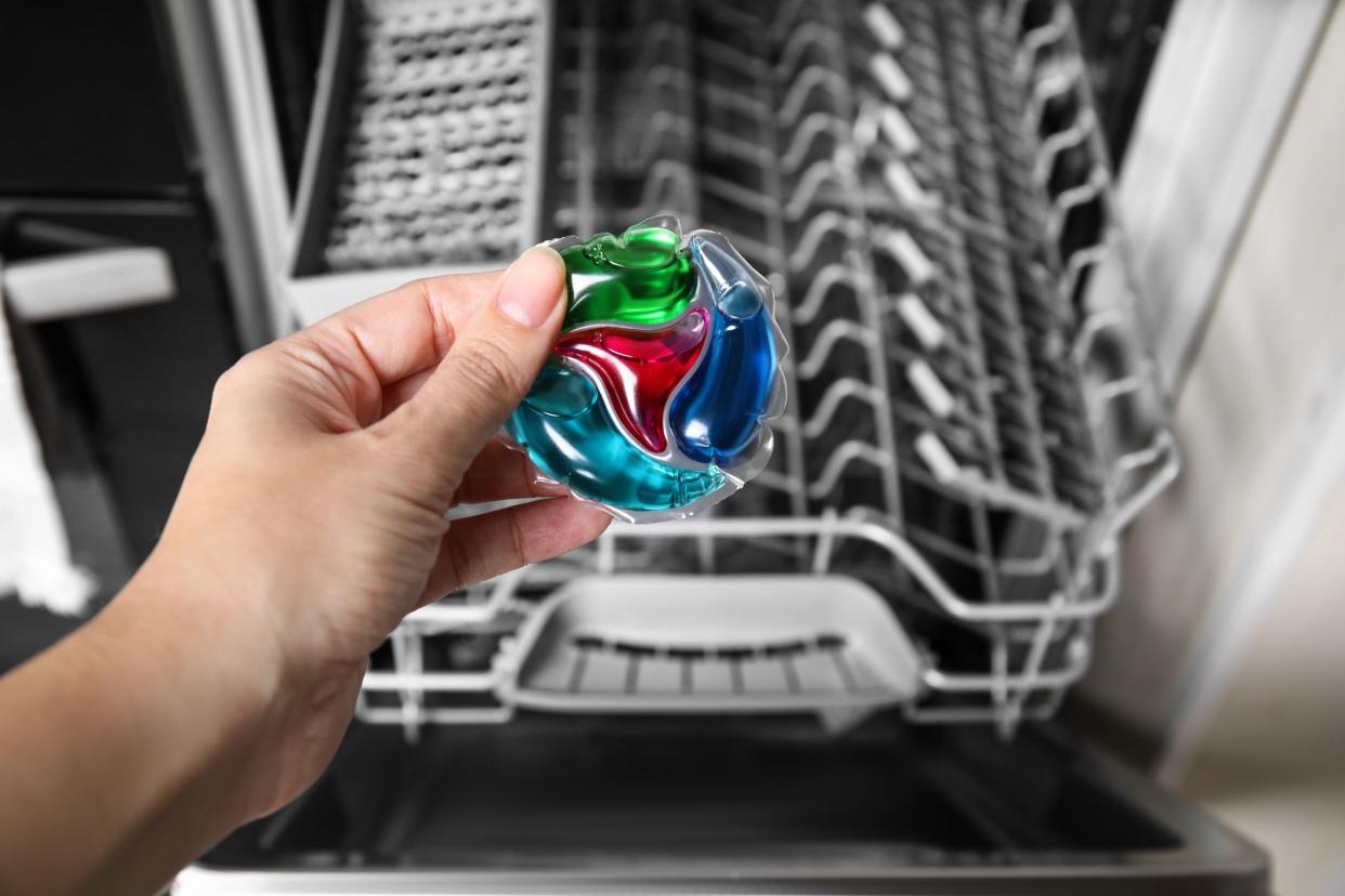 Woman putting detergent pod into open clean modern empty automatic dishwasher machine in kitchen, closeup