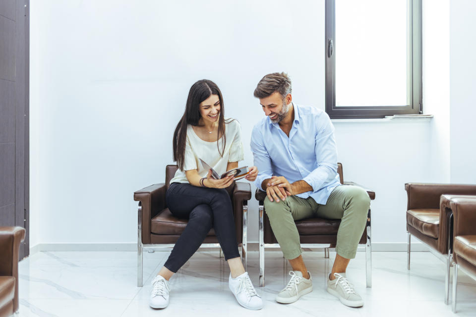 Young couple seen sitting, talking, laughing in hospital waiting room