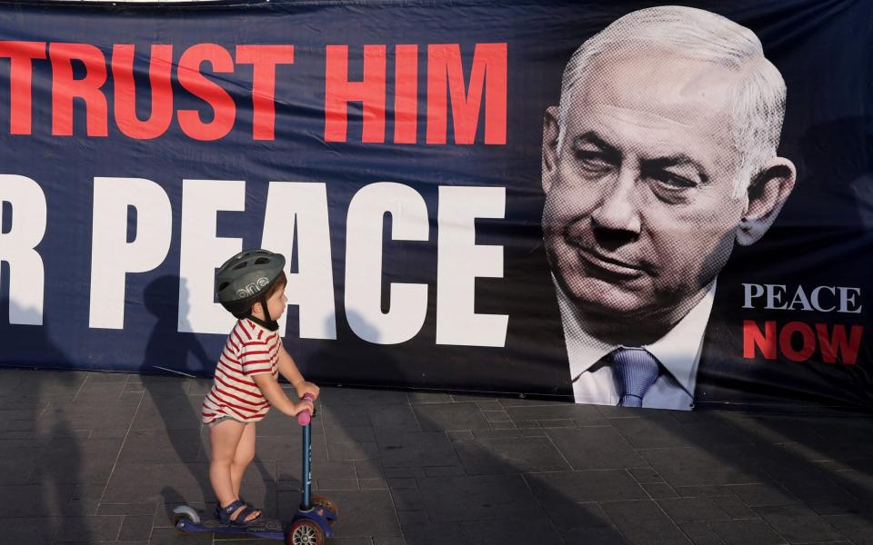 Child rides past a banner during a protest in front of the US Embassy branch office in Tel Aviv