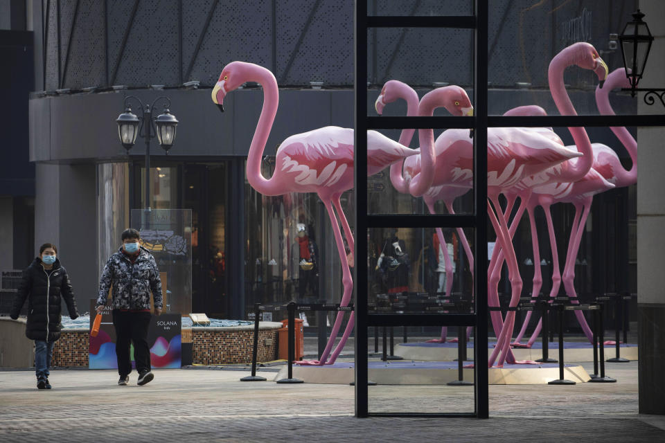 In this photo taken Wednesday, Feb. 12, 2020, residents walk through a deserted mall in Beijing, China. Millions of Chinese workers and entrepreneurs are bearing the rising costs of an anti-virus campaign that has shut down large sections of the economy. The government has imposed restrictions nationwide that have stalled travel and sales of real estate and autos. (AP Photo/Ng Han Guan)