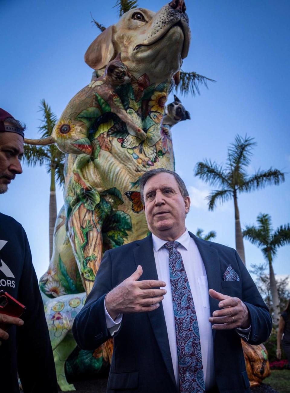 With the statue of a Labrador retriever called Chócolo by local Artist Luis Miguel Rodriguez looming in the background, Miami Commissioner, Joe Carollo, center, talks to guests at the ribbon cutting ceremony to the Dogs and Cats Walkway Sculpture Gardens at Maurice A. Ferré Park, 1075 Biscayne Blvd., Miami, on February 10, 2023.