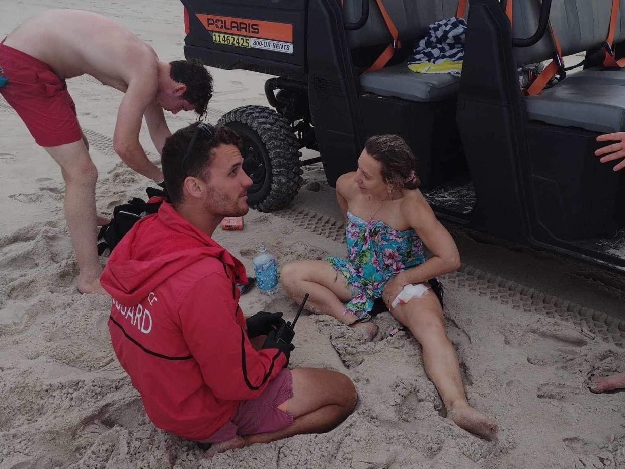 Lyudmila Emag covering her shark bite on her leg while sitting in the sand.