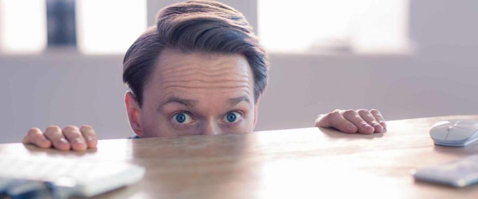 Nervous businessman peeking over desk in his office