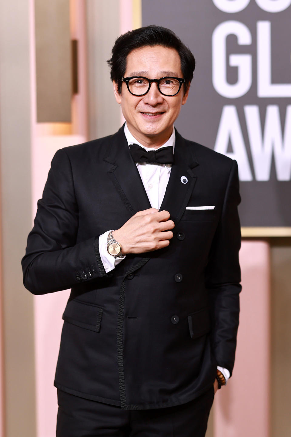 Ke Huy Quan smiles as his photo is taken at an awards show. He's wearing a suit and bowtie