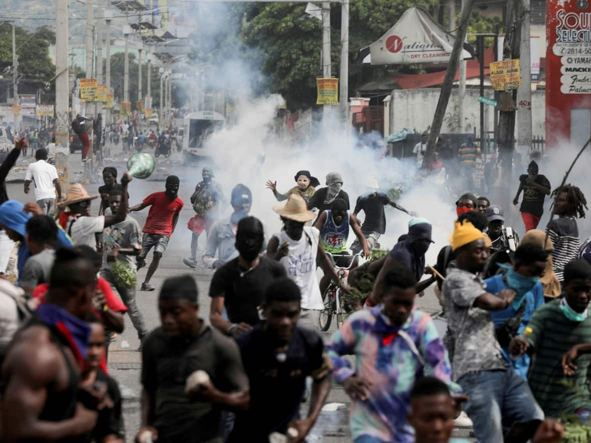 People flee while police fire tear gas during a protest demanding the resignation of Haitian Prime Minister Ariel Henry after weeks of fuel shortages, in Port-au-Prince on Oct. 10. (Ralph Tedy Erol/Reuters - image credit)