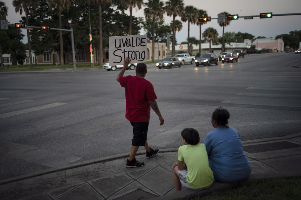 Alex Covarrubias holds up a sign at a street corner for the victims of a mass shooting that happened at Robb Elementary School, Thursday, May 26, 2022, in Uvalde, Texas. In a town as small as Uvalde, Texas, even those who didn't lose their own child lost someone. Some say now that closeness is both their blessing and their curse: they can lean on each other to grieve. But every single one of them is grieving. (AP Photo/Wong Maye-E)