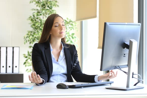 A young businesswoman meditates at her desk.