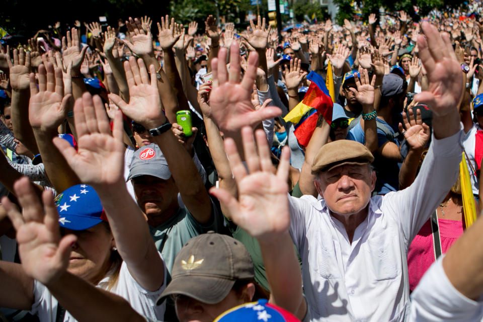 Demonstrators raise their hands in the air to show that they are unarmed and peaceful, during a protest asking for the disarmament of armed groups in Caracas, Venezuela, Sunday, Feb. 16, 2014. For the past several days, protests have rocked Caracas yielding several dead and scores of wounded in clashes between opposition protesters with security forces and pro-government supporters. (AP Photo/Alejandro Cegarra)