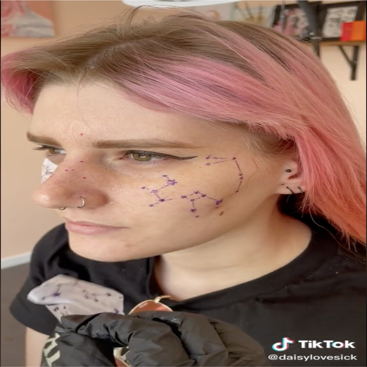Screengrab of a video by daisylovesick of her client with a constellation tattoo stencil printed on her face