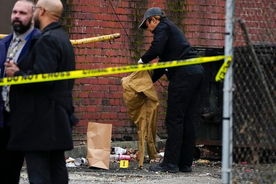 A forensics official picks up a pair of pants while collecting evidence at the site of a shooting near Edmondson Westside High School, Wednesday, Jan. 4, 2023, in Baltimore. Police say five boys, believed to be high school students on their lunch break, were shot at a shopping center and one has died. Police Commissioner Michael Harrison said two shooters opened fire, then fled behind the building.