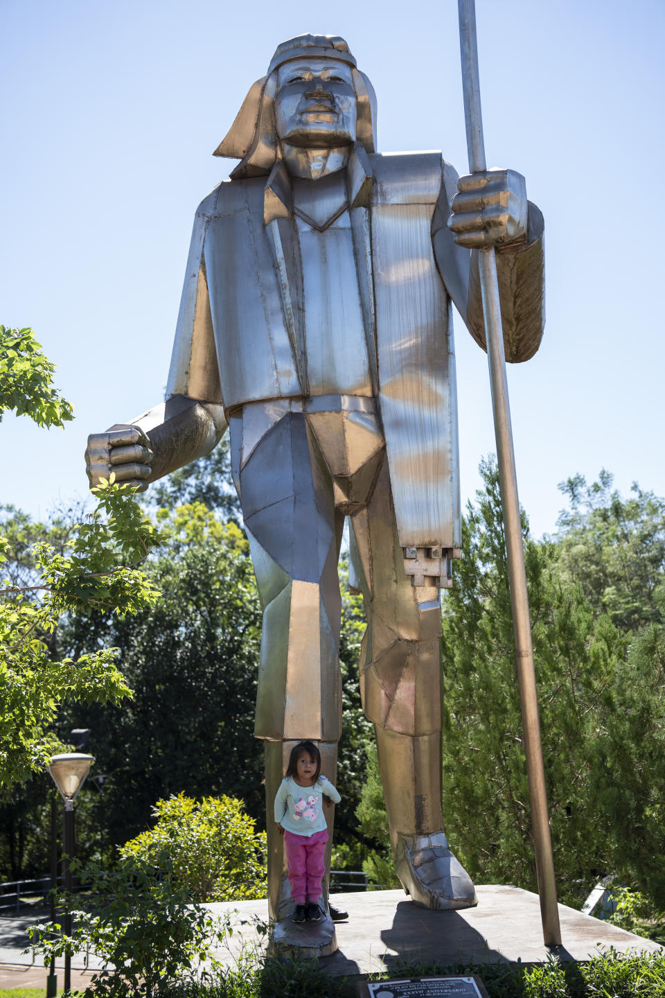 A girl plays under a monument of Andres Guacurarí, an Indigenous Guarani soldier who governed the Greater Province of the Misiones (1815 - 1819) in Andresito, in Argentina's Misiones Province, Thursday, April 18, 2024. Argentina's Misiones Province is the center of the world's maté production and was first harvested by Indigenous tribes. (AP Photo/Rodrigo Abd)