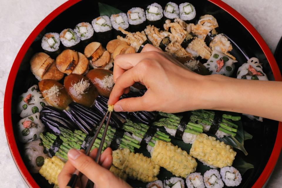 Two hands hover above a platter of sushi.