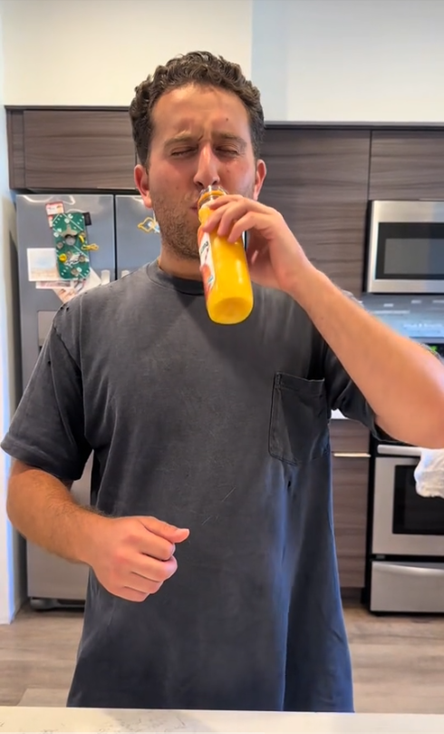 Person drinking orange juice in a kitchen