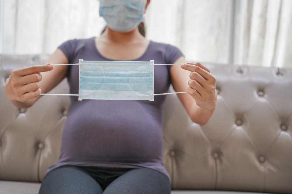 A pregnant woman wears a surgical mask to protect a COVID-19 (Coronavirus) and PM 2.5 and show a surgical mask on the abdomen to prevent infection to the fetus.