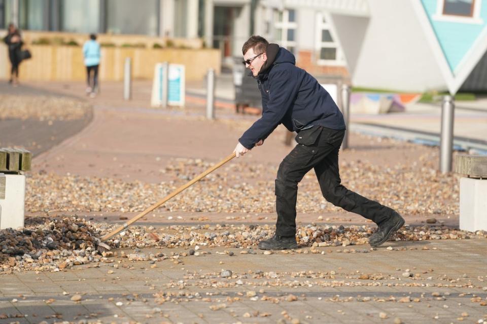 A man uses a broom to sweep pebbles back on to the beach in Sussex (Adam Davy/PA) (PA Wire)