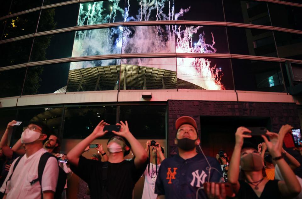 People outside the venue watch as fireworks light up the sky over the Olympic Stadium during the closing ceremony of the Tokyo 2020 Olympic Games, in Tokyo on August 8, 2021. (Photo by Yuki IWAMURA / AFP) (Photo by YUKI IWAMURA/AFP via Getty Images)