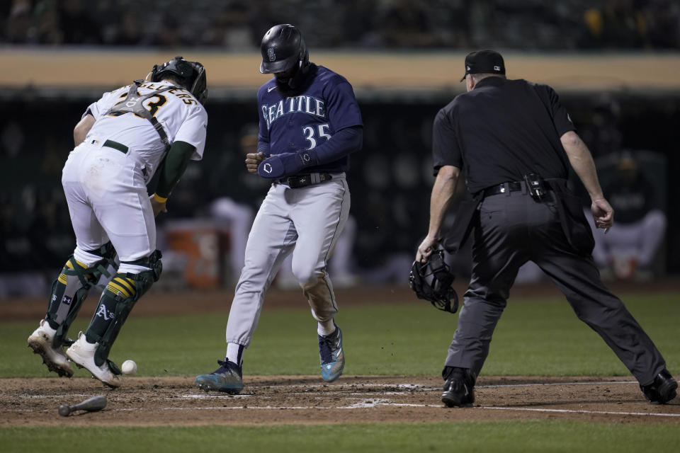 Seattle Mariners' Teoscar Hernández, center, scores next to Oakland Athletics catcher Shea Langeliers on Jarred Kelenic's single during the fourth inning of a baseball game Tuesday, Sept. 19, 2023, in Oakland, Calif. (AP Photo/Godofredo A. Vásquez)