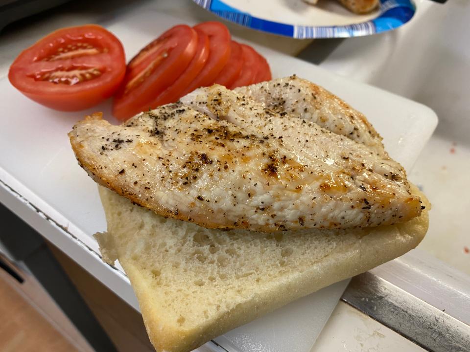 cooked chicken on bread with sliced tomatoes in the background