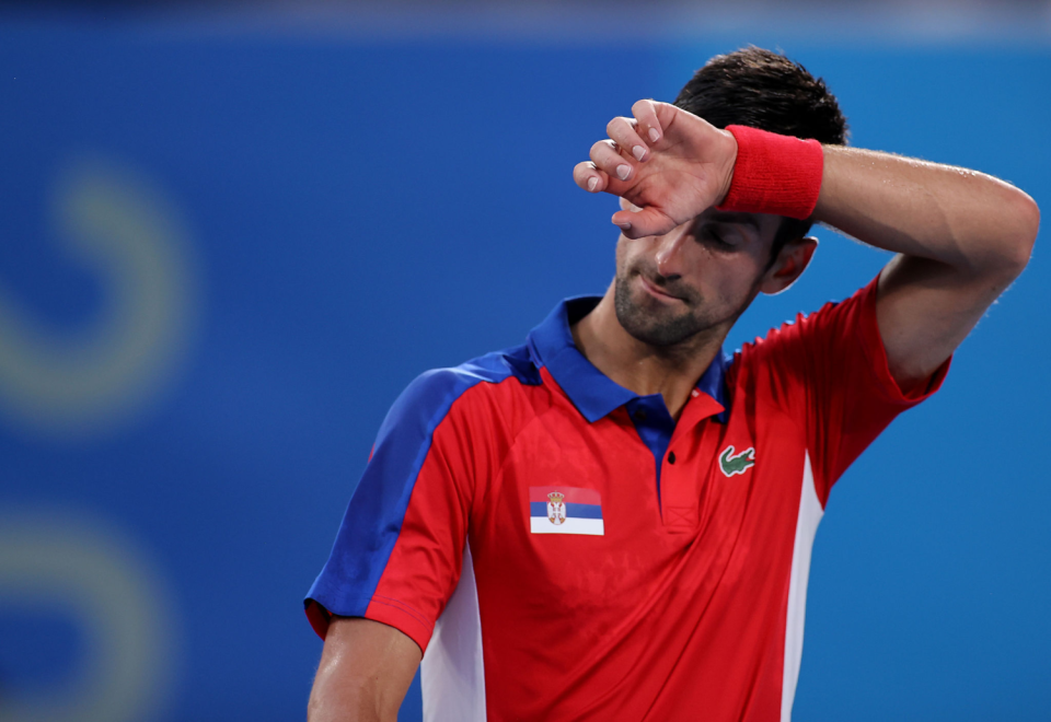 Novak Djokovic puts a sweatband-covered wrist to his forehead.