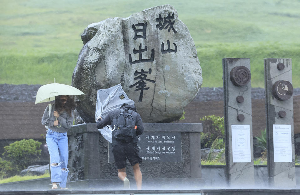 People struggle to hold onto their umbrellas in the rain and wind as the tropical storm named Khanun approaches to the Korean Peninsular, on Jeju Island, South Korea, Wednesday, Aug. 9, 2023. Dozens of flights and ferry services were grounded in South Korea on Wednesday ahead of the tropical storm that has dumped heavy rain on Japan's southwestern islands for more than a week. (Park Ji-ho/Yonhap via AP)