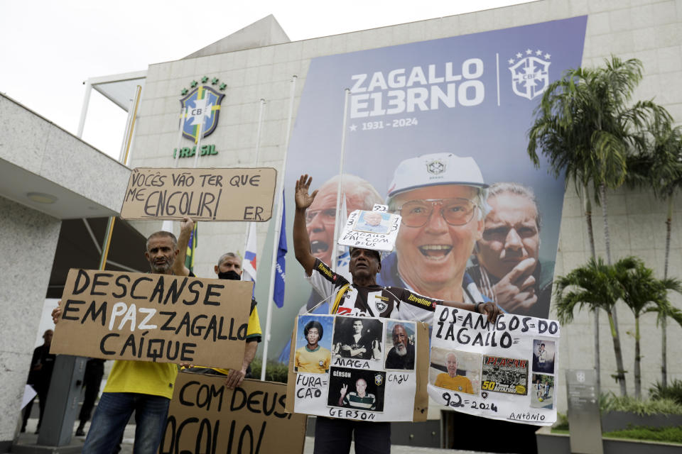 Fans of the former Brazilian soccer coach and player Mario Zagallo stand outside the Brazilian Football Confederation headquarters holding photos and banners in his honor before his funeral service in Rio de Janeiro, Brazil, Sunday, Jan. 7, 2024. Zagallo, who reached the World Cup final a record five times, winning four, as a player and then a coach with Brazil, died at the age of 92. (AP Photo/Bruna Prado)