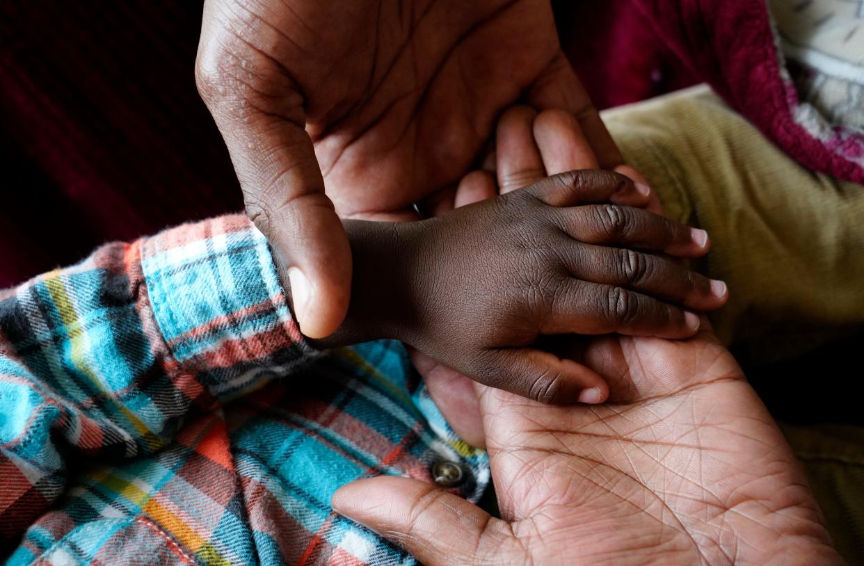 Roben, 39, along with his wife, Tatou, 28, hold hands with their son, Lewens, 18 months. The family was at the home of G3 Community Church pastor Doug Sibcy.