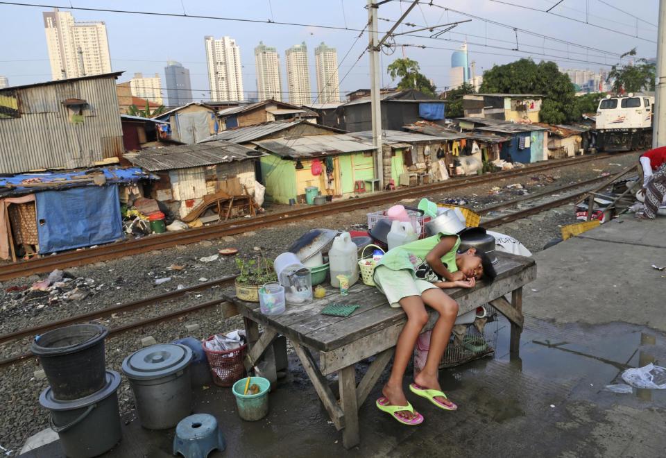 FILE - In this July 3, 2014, file photo, a young girl takes a break on a table at a slum near the main business district in Jakarta, Indonesia. A report on inequality in Indonesia says its four richest men now have more wealth than 100 million of the country's poorest people. (AP Photo/Tatan Syuflana, File)
