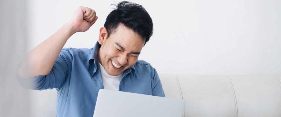 Happy Asian man using laptop in living room.