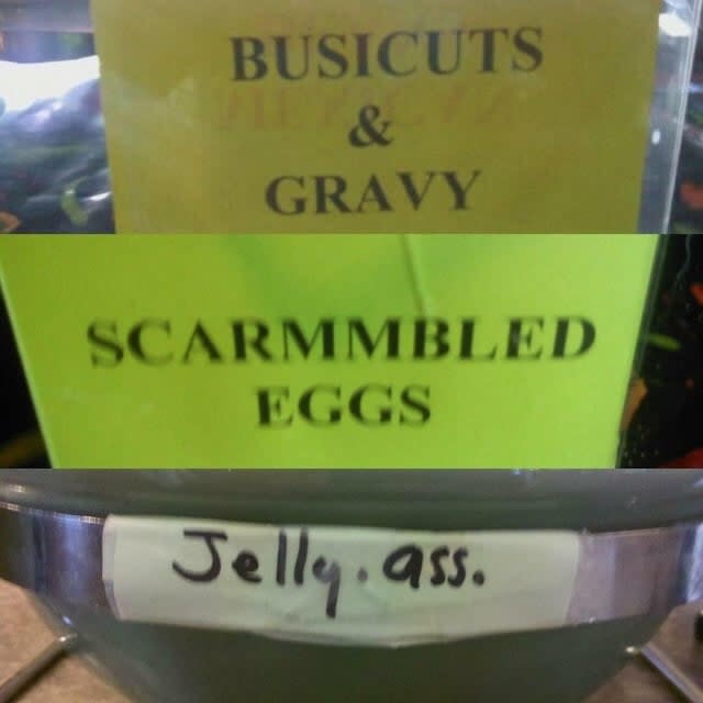 Three food signs with humorous misspellings: Biscuits as "BUSICUTS," Scrambled Eggs as "SCARMMBLED EGGS," and jelly assorted as "Jelly ass"