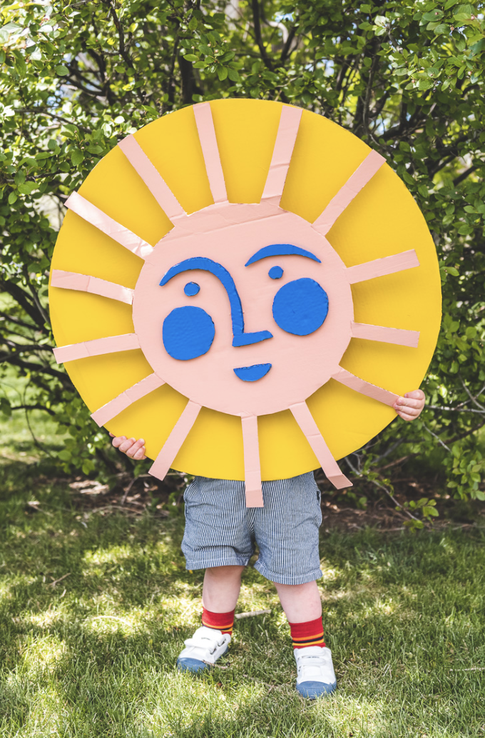 crafts for kids, child holding a large diy smiling sun made of cardboard outdoors