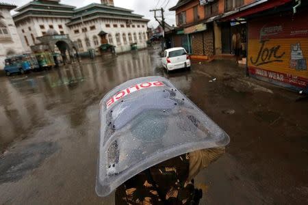A policeman uses his shield to cover himself from rain as he patrols a deserted road during a curfew in downtown Srinagar July 27, 2016. REUTERS/Danish Ismail