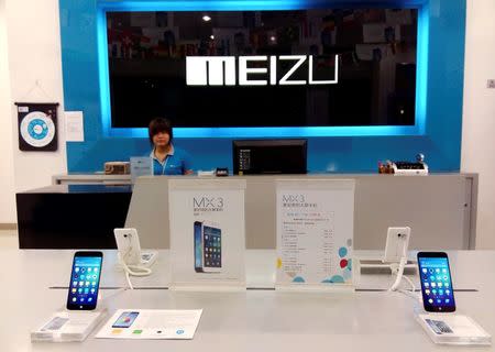 A shop assistant waits for customers at a Meizu store as Meizu MX3 smartphones are seen on display in the foreground, in Shenzhen, Guangdong province June 16, 2014. REUTERS/Stringer