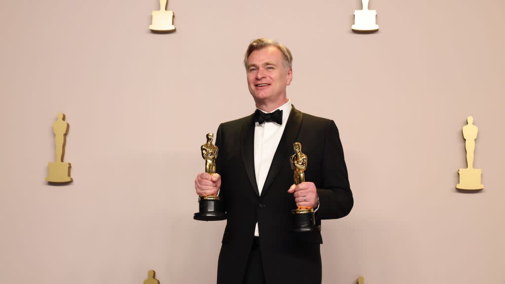 christopher nolan holding two oscar stutuettes and smiling