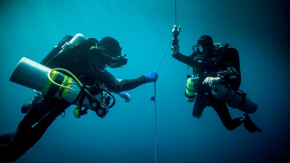 Underwater view of two technical divers using rebreathers device to locate shipwreck.