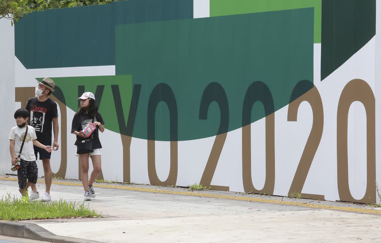 Tres personas pasan junto a carteles de promoción de los Juegos Olímpicos de Tokio.