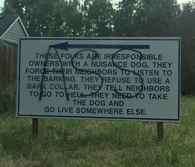 Close-up of sign talking about neighbors who are "irresponsible owners with a nuisance dog" because "they force their neighbors to listen to the barking," with "ASS" written across it in large letters