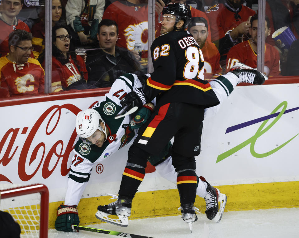 Minnesota Wild forward Marcus Foligno, left, is checked by Calgary Flames defenseman Jordan Oesterle during the second period of an NHL hockey game, Tuesday, Dec. 5, 2023 in Calgary, Alberta. (Jeff McIntosh/The Canadian Press via AP)