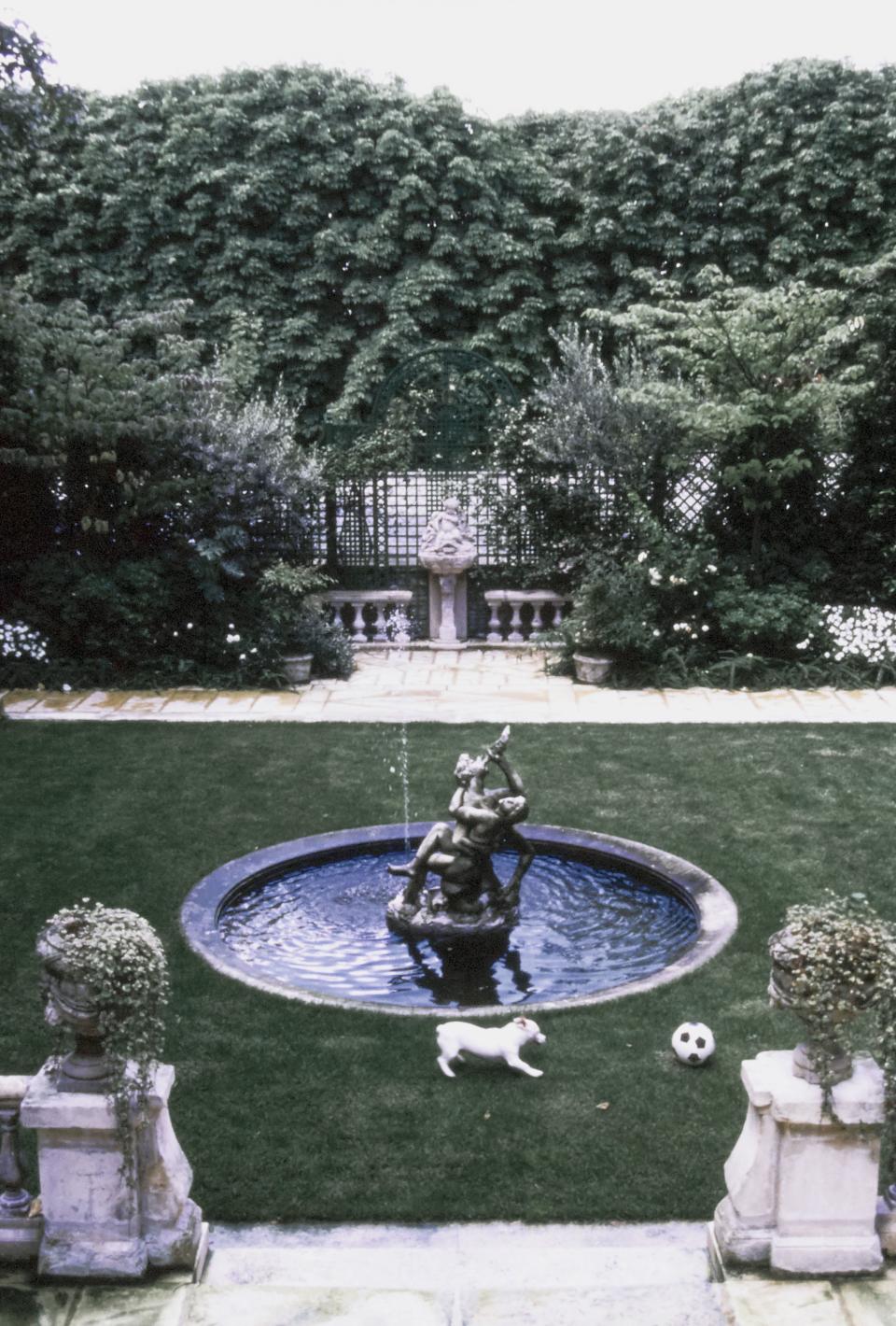 The formal garden and water fountain at fashion designer Emanuel Ungaro’s Left Bank, Paris, France, home that he shares with his wife, Laura Ungaro (née Bernabei) and their daughter, Cosima. Olli, Cosima's Jack Russell Terrier dog, runs in the rear garden chasing a soccer ball.