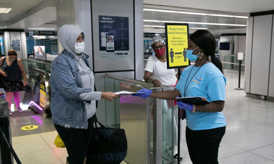 Shaquanna Parnell, right, with the Mayor's Office of Public Engagement, hands an information leaflet to a passenger arriving at Amtrak's Penn Station on Aug. 6, 2020 in New York City. At the time, travelers from states with high COVID-19 infection rates were required to quarantine for 14 days after arriving in New York.