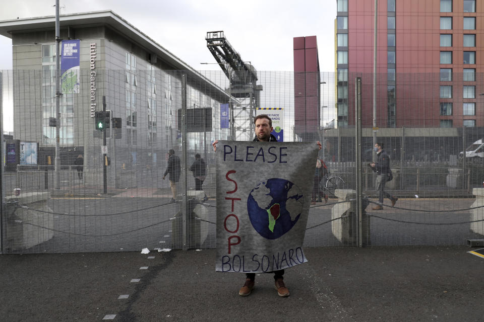 A climate protester holds a banner against Brazilian President Jair Bolsonaro by the security fencing outside the Scottish Event Campus, the venue for the COP26 U.N. Climate Summit in Glasgow, Scotland, Tuesday, Nov. 2, 2021. The U.N. climate summit in Glasgow gathers leaders from around the world, in Scotland's biggest city, to lay out their vision for addressing the common challenge of global warming. (AP Photo/Scott Heppell)