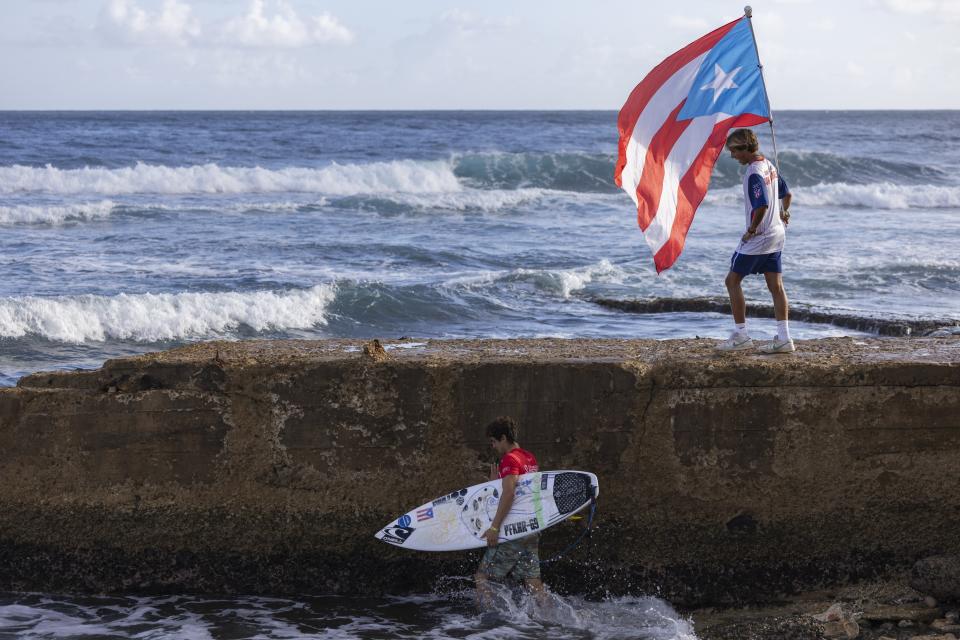 El puertorriqueño Dwight Pastana lleva su tabla hacia el agua en los Juegos Mundiales de Surf de la ISA, el clasificatorio a los Juegos Olímpicos de París 2024, en la playa La Marginal, en Arecibo, Puerto Rico, el jueves 29 de febrero de 2024. (AP Foto/Alejandro Granadillo)