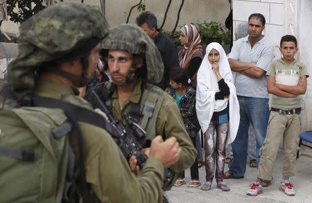 Palestinians stand outside their house as Israeli soldiers take part in an operation to locate three Israeli teens near the West Bank City of Hebron June 21, 2014. REUTERS/Mussa Qawasma