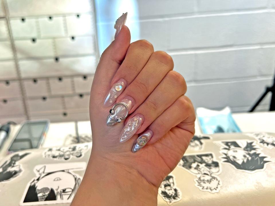hand posing to show off a silver chrome manicure with extensions and charms