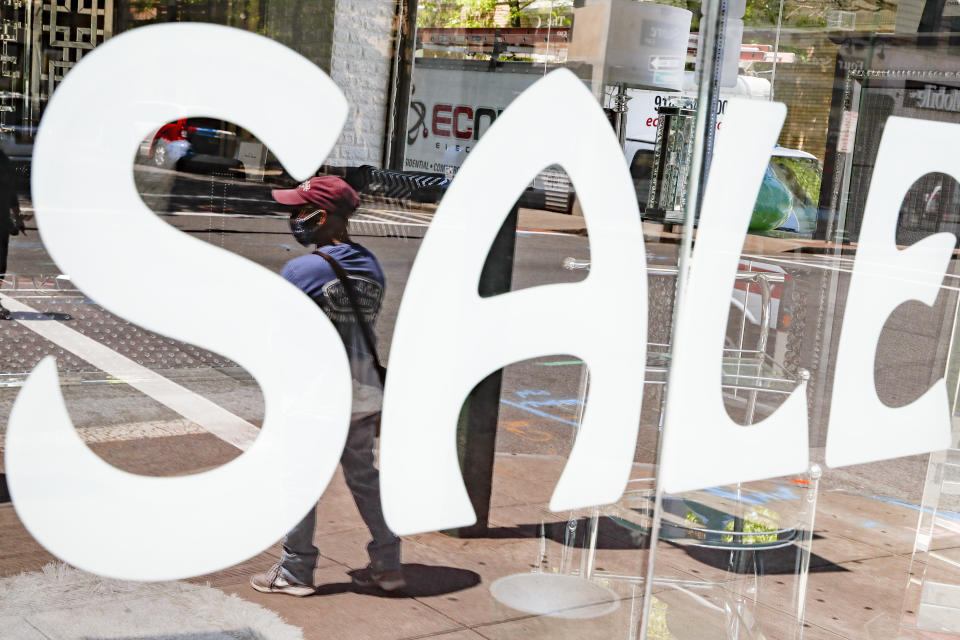 A pedestrian wearing a protective mask waits to cross Main Street beside a shuttered business storefront, Tuesday, May 26, 2020, in New Rochelle, N.Y. (AP Photo/John Minchillo)